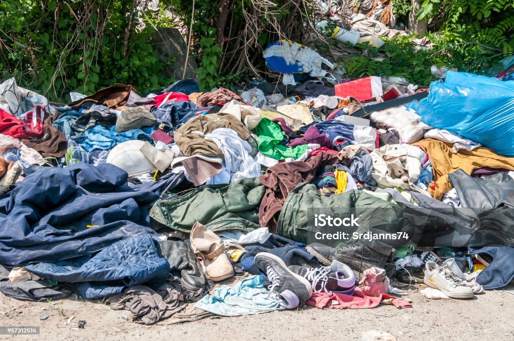 Pile of old clothes and shoes dumped on the grass as junk and garbage, littering and polluting the environment Clothing Stock Photo