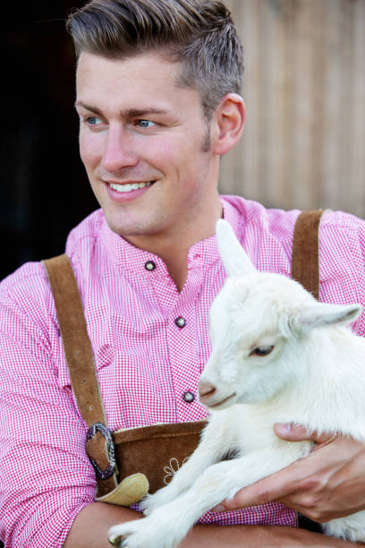 istock blond bavarian man holding a little white goat 957329144