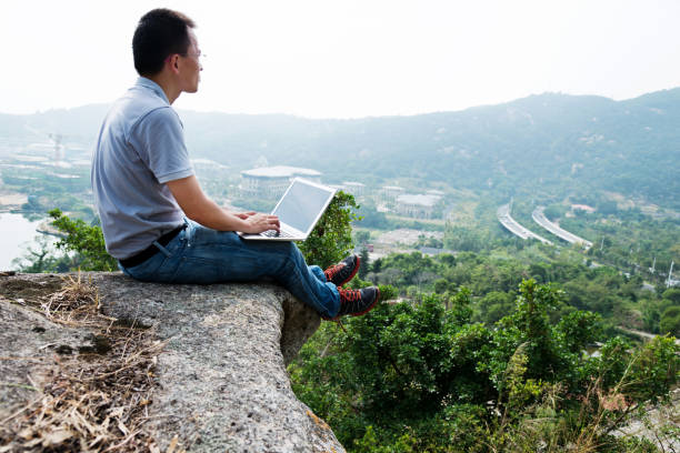 istock Man sitting at the edge of a cliff using laptop 957331662