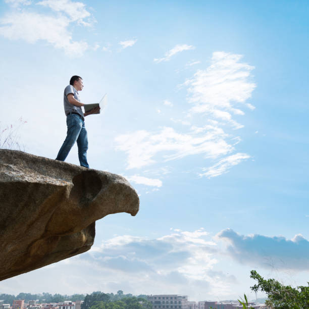 istock Man standing at the edge of a cliff using laptop 957332028