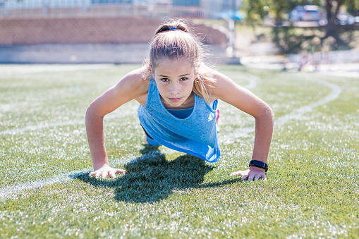 Sporty girl doing push up front view on sports field looking up at camera, focused.