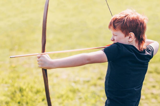 istock Redheaded boy aiming for a target with a bow arrow 957350550