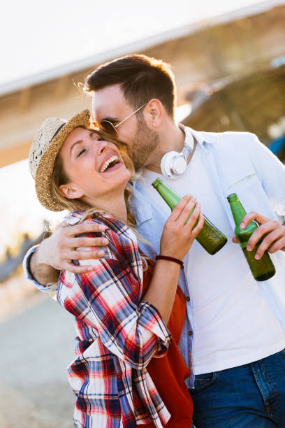 istock Happy couple smiling and drinking beer at beach 957350950