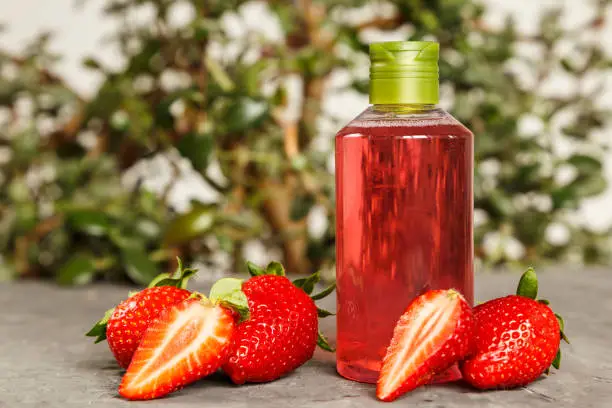 Natural cosmetics ingredients, for a body and hair from strawberry. Red liquid in a transparent bottle. Strawberry oil, shampoo, shower gel.