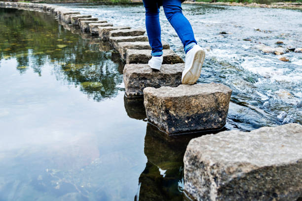 mulher cruzando as pedras de piso em um rio - stepping stone stone stepping footpath - fotografias e filmes do acervo