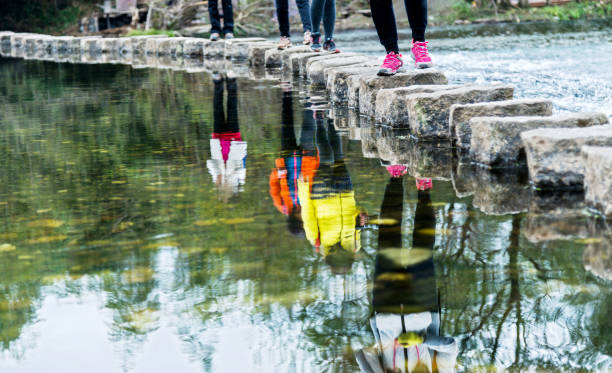 quatre femmes traversant des pierres de gué sur une rivière - stepping stone stone stepping footpath photos et images de collection