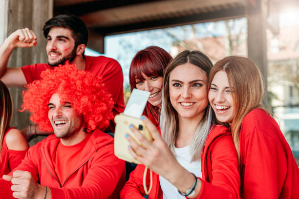 istock Fans at stadium together taking selfie with instant print camera 957360428