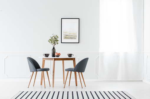 Small dining furniture set and a striped rug in a minimalist white interior with art above the table