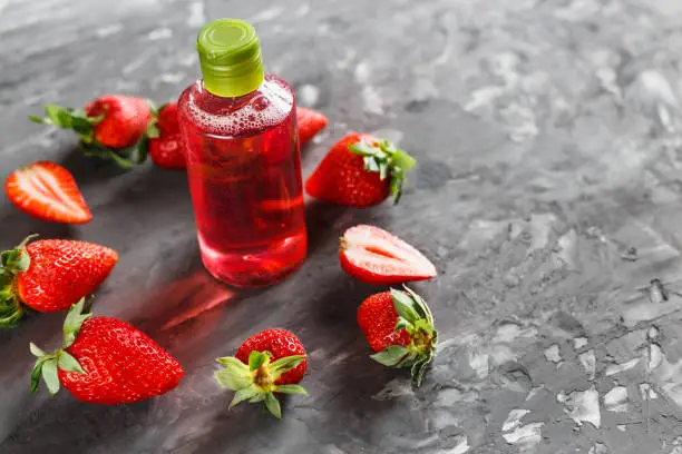 Natural cosmetics ingredients, for a body and hair from strawberry. Red liquid in a transparent bottle. Strawberry oil, shampoo, shower gel. Against a dark background