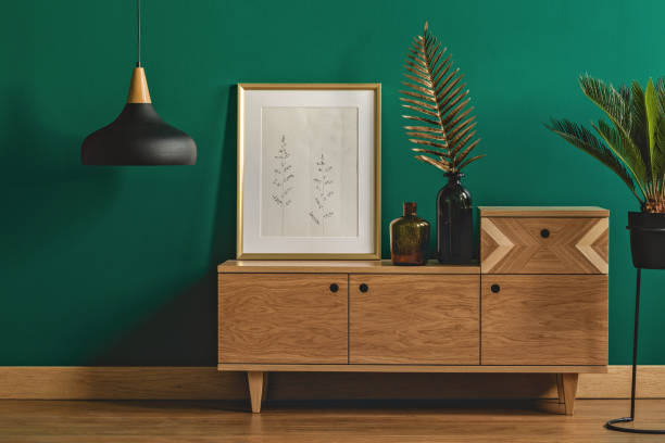 Stylish dark green interior Industrial pendant light next to a stylish dresser and an art poster in a golden frame by a dark green wall of a modern bedroom interior dresser stock pictures, royalty-free photos & images
