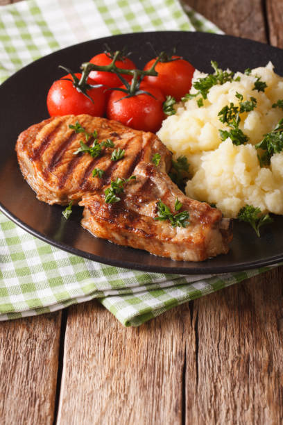 istock Grilled pork loin with mashed potatoes and tomato close-up. Vertical, rustic 957376348