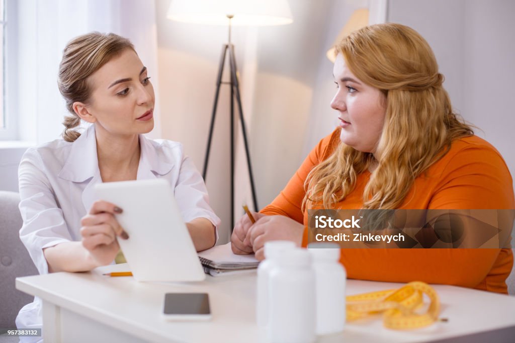 Serious skilled nutritionist talking with a stout woman My profession. Determined experienced nutritionist talking with a fat woman and holding her tablet Diabetes Stock Photo