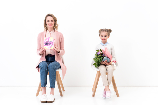 mother and daughter sitting on chairs and looking at camera on happy mothers day