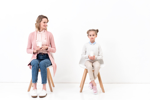 mother and daughter sitting on chairs with glasses of milk on white