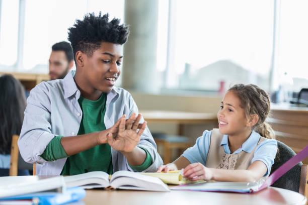 High school student tutoring younger student Confident teenage male high school student tutors an elementary school student after school. The high school student is helping the student with a math assignment. He is counting on his fingers. high school student classroom education student stock pictures, royalty-free photos & images