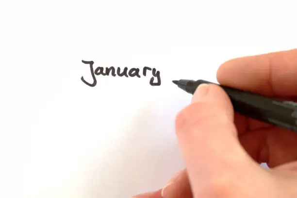 January, black handwritten word on white paper, hand holding pen
