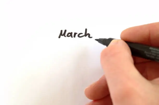 March, black handwritten word on white paper, hand holding pen