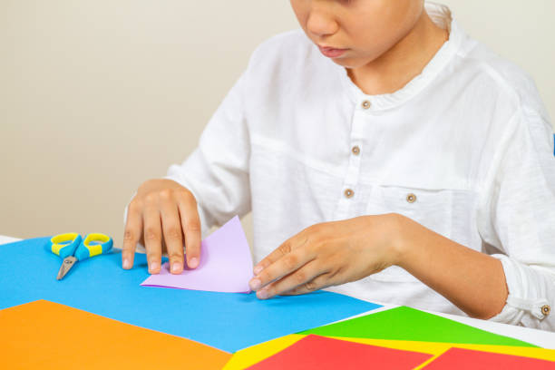 istock Child cutting colored paper with scissors at the table 957414792
