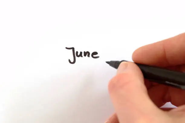June, black handwritten word on white paper, hand holding pen