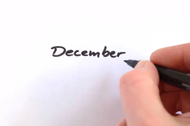December, black handwritten word on white paper, hand holding pen