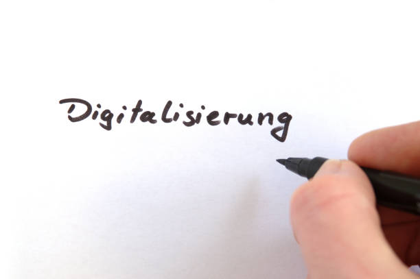 istock Digitalisierung (German for Digitalization), black handwritten word on white paper, hand holding pen 957417106