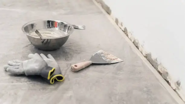 Bowl with mixed powder putty, putty knife and gloves on the floor. Wall spackling equipment