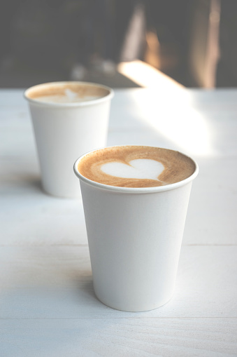 Two simple white paper cups of coffee take-away on white wooden table.