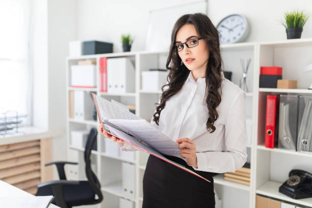 istock Beautiful young girl stands in the office thumbs a folder with documents. 957454732