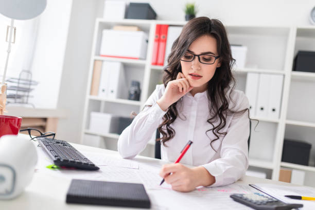 istock Young girl sits at office desk and fills documents with her left hand. 957457894