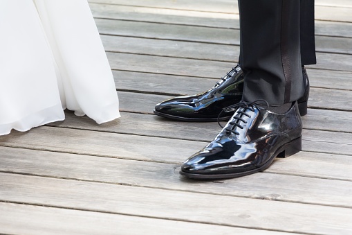 The man and the woman wearing luxury lifestyle bridal dress, suit and shoes. The Male shoe luster is polished. Wooden floor copyspace.