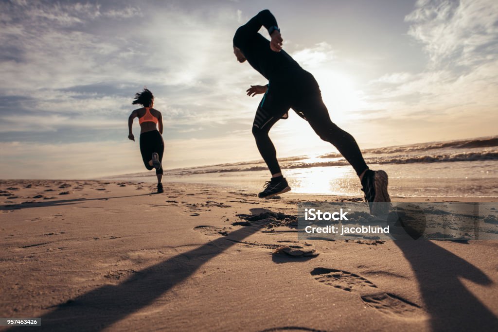 Fit people sprinting on the beach Rear view of two people sprinting on the beach. Man and woman doing running training on the shore in morning. Beach Stock Photo