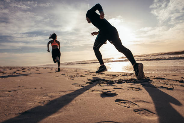 Fit people sprinting on the beach Rear view of two people sprinting on the beach. Man and woman doing running training on the shore in morning. healthy lifestyle women outdoors athlete stock pictures, royalty-free photos & images