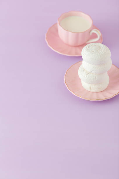istock Pastel violet and pink vertical banner with copy space - white zephyr on plate and cup of coffee with milk. 957479218