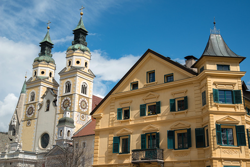 Yellow building in brixen at sunlight. No people visible. Blue sky and cathedral visible.