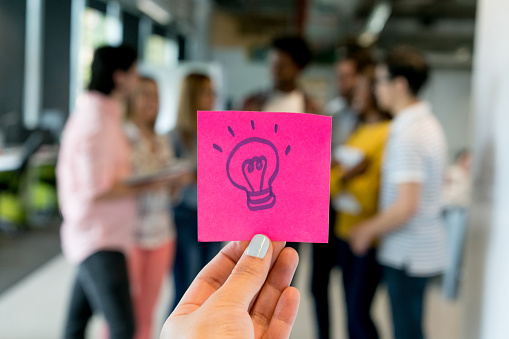Unrecognizable person holding a sticky note with a lightbulb symbolizing innovation - business concepts