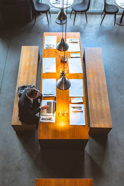 istock High Angle View of a Handsome Businessman Using Mobile Phone and a Laptop in a High-End Restaurant 957539548