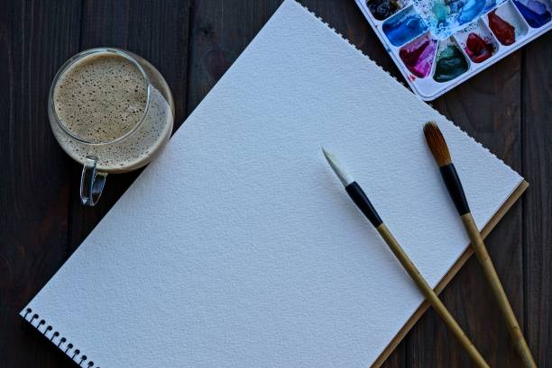 istock white empty notebook with brushes and a set of colors and a cup of coffee on a black table 957549930