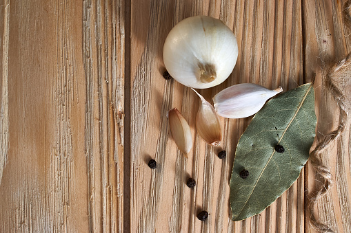 onion, garlic, black pepper and bay leaf on a wooden table