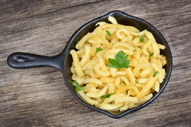 Spaetzle with butter and parsley in a iron pan on rustic wood table