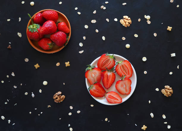 Ripe strawberries and crumbled granola on a black table.