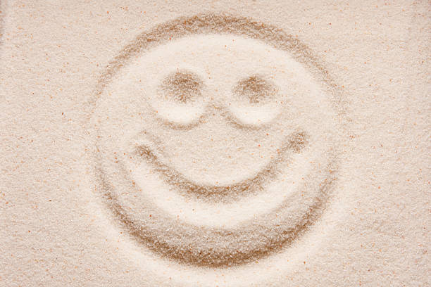 A close up of a woman's hand and she draws a yin-yang symbol in went sand at Point Pelee National Park, Canada.