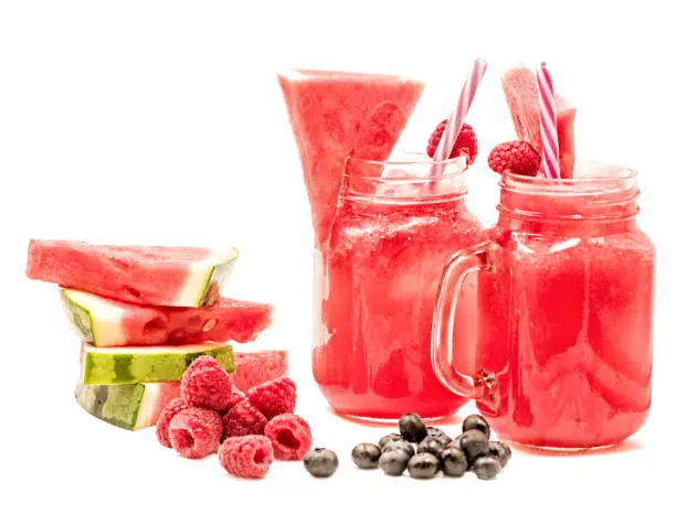 Photo of watermelon smoothie in a mason jar decorated with a slice of watermelon, raspberries, blueberries and ice cubes isolated on white background. fruit smoothie with a drinking straw isolated