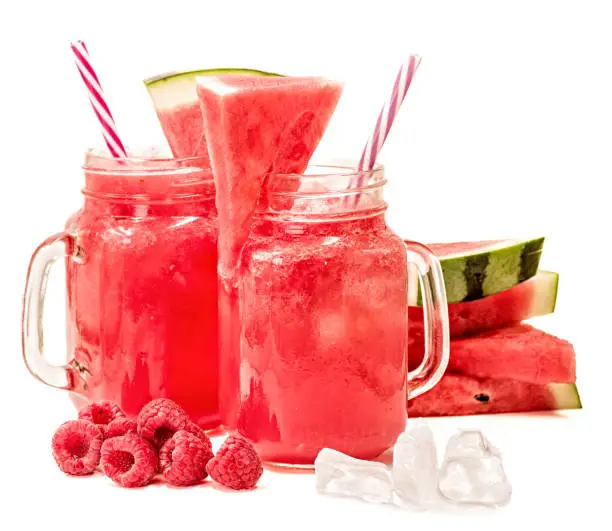 Photo of watermelon smoothie in a mason jars decorated with a slice of watermelon, raspberries and ice cubes isolated on white background. fruit smoothie with a drinking straw isolated