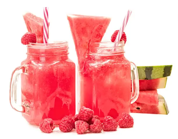 Photo of watermelon smoothie in a mason jar decorated with a slice of watermelon, raspberries and ice cubes isolated on white background. fruit smoothie with a drinking straw isolated