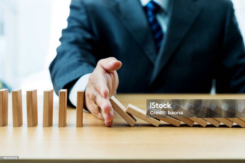 Businessman hand stopping falling blocks on table Businessman hand stopping falling blocks on table. Domino Effect Stock Photo