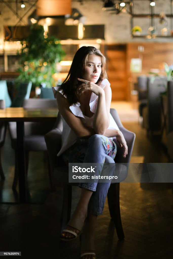 Stylish woman sitting at cafe and wearing white blouse with ethnic jeans Stylish woman sitting at cafe and wearing white blouse with ethnic jeans. Concept of fashion and beauty. Luxury Stock Photo