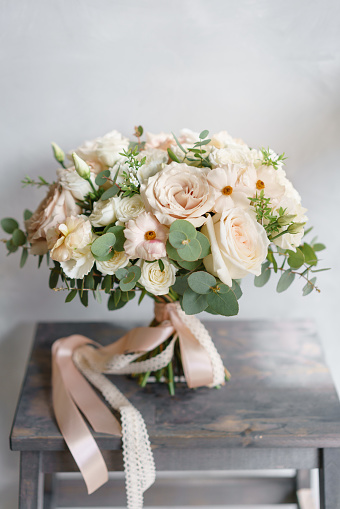 Wedding bouquet of white roses and buttercup on a wooden table. Lots of greenery, modern asymmetrical disheveled bridal bunch. Pastel color