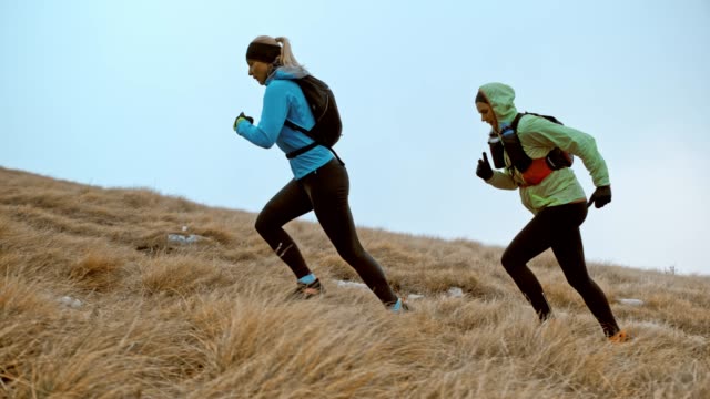 SLO MO Two female runner running up a grassy slope on a cold day