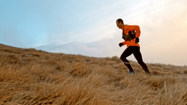 Slow motion wide handheld side shot of a male runner running up the mountain on a grassy slope. Shot in Slovenia.