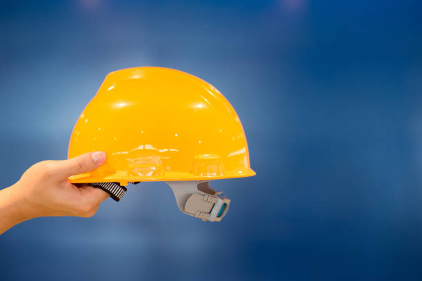 istock Male engineer hand holding personal yellow protective safety helmet on blue background 957669642